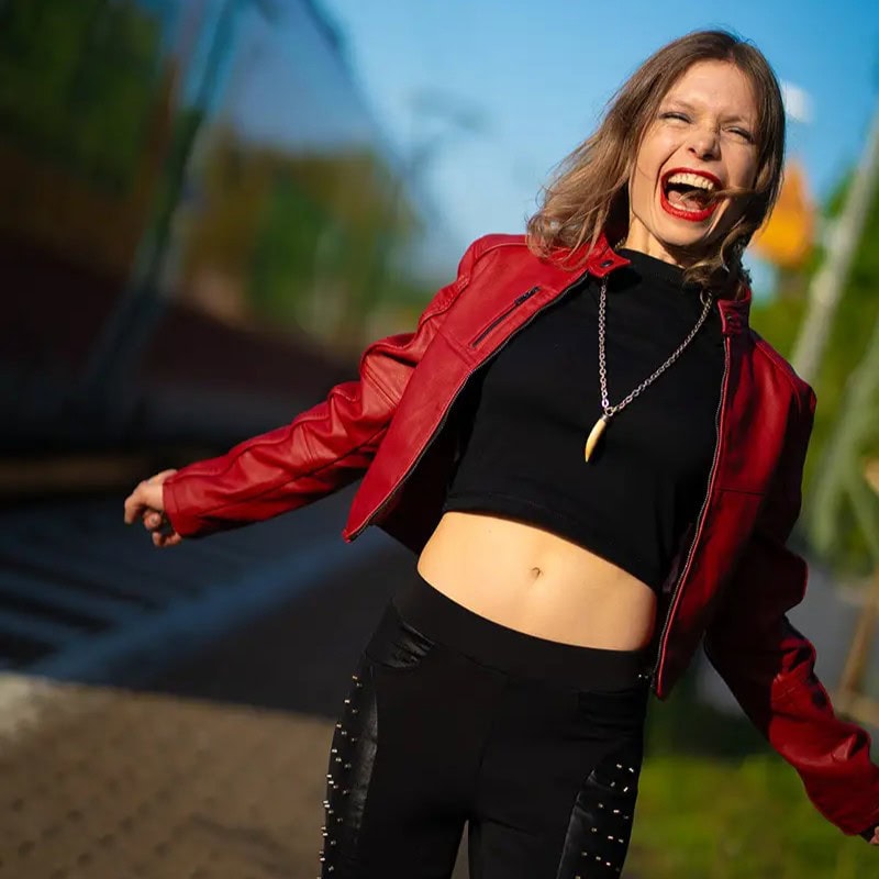 Junge Frau mit roter Jacke und schwarzem Top beim Tanzen auf Bahnstrecke.