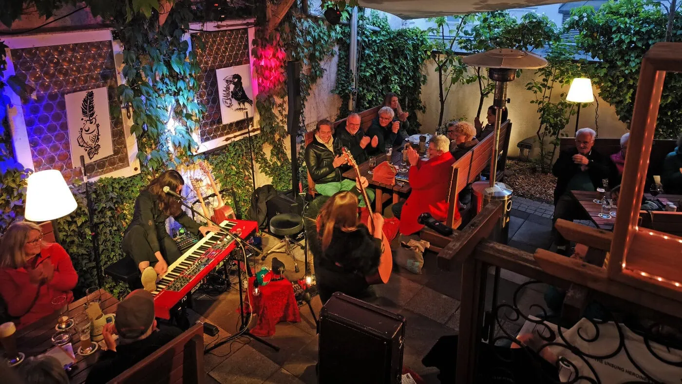 Teaser zu Schlafen mit Musik mit einem Konzertfoto aus dem Biergarten des Atelier Teufelsbäck mit Fischer & Rabe sowie Publikum.